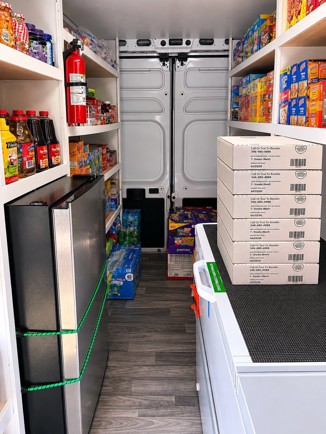 Inside the FreshDrop HTX truck — shelves stocked with packaged groceries, snacks, juices, a refrigerator on the left, and stacked frozen meat boxes on the right